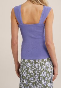 Sääntöjen mukaan sovitettu, olkaimeton toppi laventelin värisenä neuleena, leveillä olkaimilla ja neliömäisellä selkäosalla. Yhdistetty kukalliseen vihreään hameeseen, jossa on valkoisia yksityiskohtia.