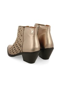 Botines de bronce con diseño superior trenzado, detalles metálicos suaves y un tacón grueso negro. Cierre lateral con cremallera para poner y quitar fácilmente.