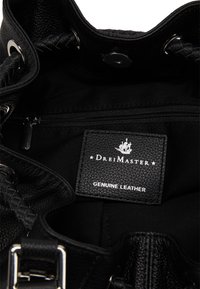 Intérieur d'un sac à main en cuir véritable noir montrant une étiquette cousue avec un logo de bateau et le nom de la marque "Drei Master" sous la poche zippée.
