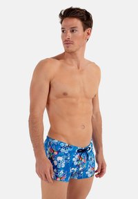 Blå blomstrede badeshorts med snor i taljen, der har et levende mønster af blomster og abstrakte former, lavet af letvægtsmateriale.
