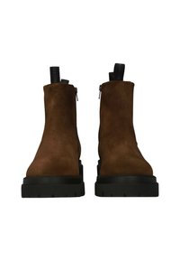 Botas Chelsea de ante marrón con suela negra gruesa, que presentan cremalleras laterales y tiradores en la parte trasera para facilitar su uso.