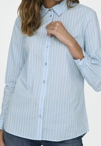 Light blue long-sleeve button-up shirt with vertical stripes in various pastel colors. Features a classic collar and standard button closure.