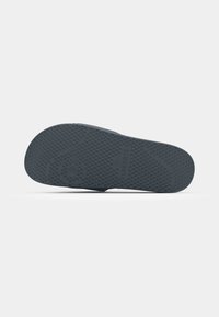 Lacoste shoe sole in dark gray rubber, featuring a textured surface with circular and patterned grips for traction and stability.