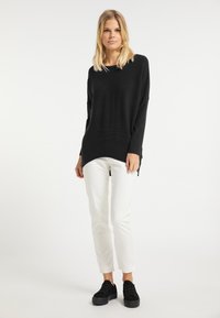 Maglione nero a maniche lunghe con finitura testurizzata, abbinato a pantaloni bianchi slim-fit e sneakers nere, che mostrano una vestibilità rilassata e spacchi laterali.