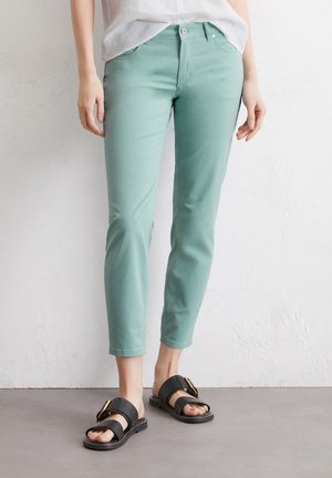Pantalons cropped vert menthe en coton, dotés d'une fermeture à bouton et de poches, associés à des sandales noires avec des accents en métal doré.