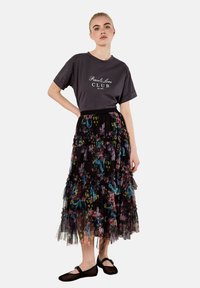 Szara koszulka z napisem "Pokój i Miłość KLUB" w połączeniu z czarną spódnicą z tiulu z kolorowymi kwiecistymi wzorami. Całość dopełniają czarne płaskie buty.