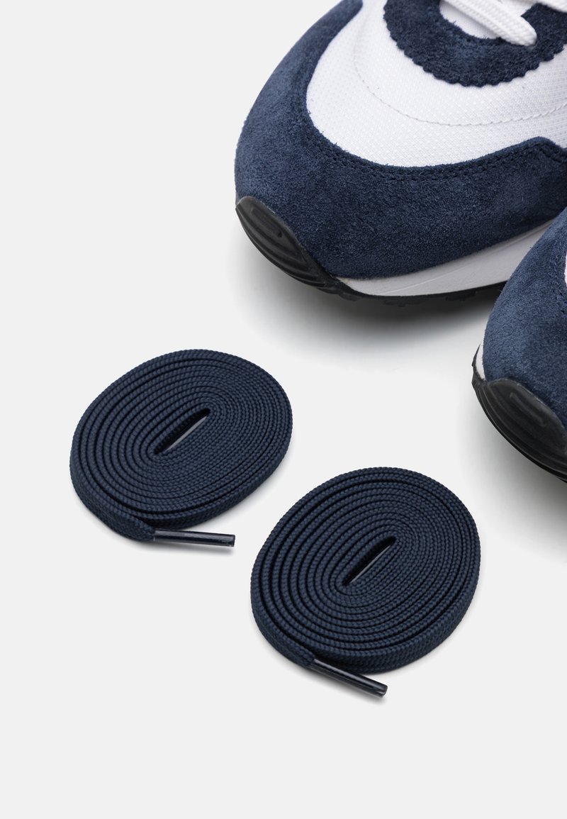 Zapatillas de ante y malla en color azul marino con acentos blancos, con cordones redondos dispuestos a su lado, mostrando textura y detalle.