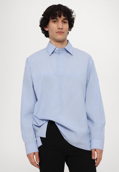 Sinise ja valge triibuline pikkade varrukatega särk, millel on nööbiga krae ja mugav lõige; rinnal on horisontaalne õmblus.