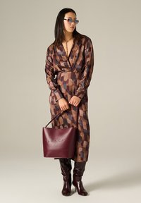 Robe marron à motifs avec des manches longues, associée à des bottes bordeaux jusqu'aux genoux et un sac à main assorti. Les accessoires incluent des lunettes de soleil et un collier en chaîne.