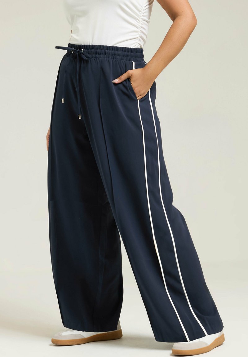 Pantalones de pierna ancha en azul marino con rayas laterales blancas, cinturilla elástica y cordón. Fabricados con tejido suave, cuentan con bolsillos laterales.