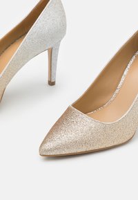 Chaussures à talons aiguilles pailletées en or et en argent. Design à bout pointu avec surface texturée et talon stiletto élégant. Couleur intérieure neutre.