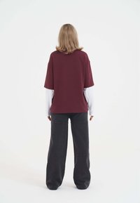 Burgundowa, oversize koszulka z krótkim rękawem, nałożona na białą koszulę z długim rękawem. Połączona z szerokimi, ciemnoszarymi spodniami.