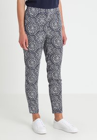 Pantalon à motifs marins avec des designs floraux blancs, coupe ajustée et tissu extensible. Associé à des baskets blanches pour un look décontracté.