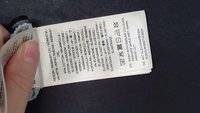 Main tenant une étiquette d'entretien du tissu montrant les instructions de lavage, la composition des fibres et les symboles d'entretien sur un fond noir.
