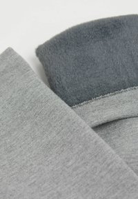 Grå bomuldsstof overlapper med et blødt, fuzzy grå materiale. Kanterne er ufærdige og viser en rå kant ved forbindelsespunktet.