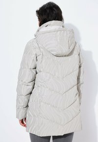 Chaqueta acolchada gris con un patrón de flechas, que cuenta con una capucha y una textura brillante. El diseño tiene rayas horizontales en el material.
