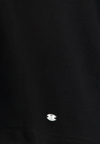 Black cotton shirt featuring a silver oval logo tag with "KEY LARGO" text. Smooth texture with visible stitching along the hem.