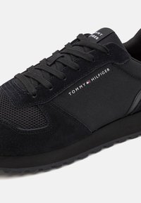 Baskets noires Tommy Hilfiger avec dessus en mesh et daim, lacets noirs et logo de la marque sur le côté et la languette.