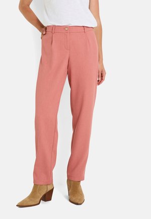 Pantalones ajustados de un rosa claro con una textura suave, que presentan pliegues en la parte delantera, cierre de botón y bolsillos laterales. Combinados con botas de tobillo de tacón color marrón.