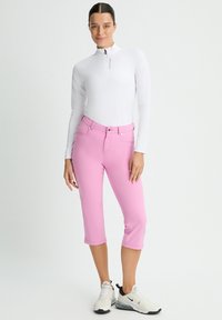 Vit långärmad zip-up tröja i kombination med rosa capribyxor, med bältesöglor och framfickor, kompletterat med vita och svarta sneakers.