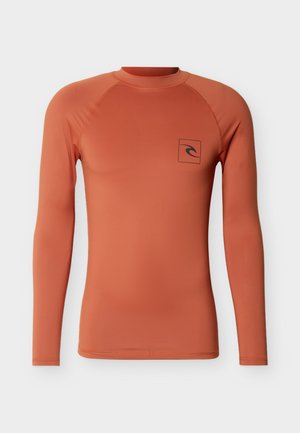 Chemise ajustée à manches longues orange rouille avec col rond et petit logo noir en forme de vague sur le côté gauche de la poitrine, sur un fond clair uni.