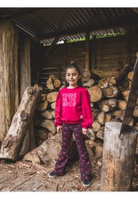 Rode sweat met de tekst "FOCUS ON THE GOOD", gecombineerd met patterned leggings met hartjes. Op de achtergrond gestapelde houtblokken en een houten constructie.