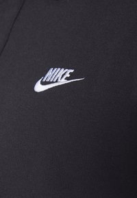 Černé tričko vyrobené z bavlněné tkaniny s bílým vyšívaným logem Nike. Textura je hladká, má přiléhavý střih a límec typu crew neck.