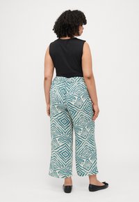Black sleeveless top paired with lightweight, wide-leg pants featuring a turquoise geometric pattern on a cream background. Black flats.