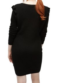 Svart räfflad klänning med lång ärm, med volangdetaljer på axlarna och en figurnära siluett.