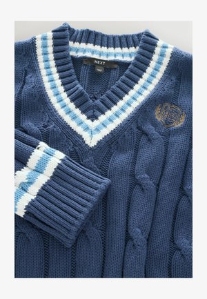 Tumši zils džemperis ar rakstu adījumu un V veida kaklu, apkaklītē un aprocēs ar baltām un gaiši zilām svītrām, kā arī izšūtu logotipu.