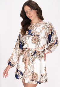 Blumenmuster-Kleid mit weißem Grund, marineblauen Akzenten und Pfirsichtönen. Verfügt über eine lockere Passform, lange Ärmel und eine gebundene Taille.