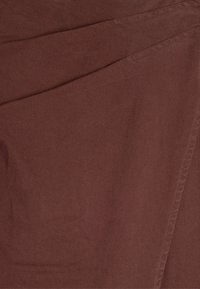 Brązowa tkanina o teksturowanym wykończeniu, z ukośnym wzorem i subtelnymi detalami ściegów. Materiał wydaje się miękki i trwały.