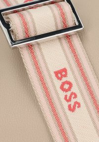 Prodotto in pelle beige con una tracolla a righe beige e rosa, caratterizzato da una fibbia rettangolare argentata e il testo "BOSS" in rosso.