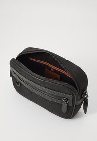 Schwarze Stoff-Crossbody-Tasche mit einem strukturierten Muster, ausgestattet mit einem oberen Reißverschluss, einer Außentasche mit Reißverschluss und einem kontrastierenden orangen Innenfutter.
