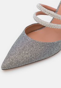 Pumps med spetsig tå och glittrig silverutsida samt dubbla glittrande remmar över foten. Mjuk rosa innerfoder.