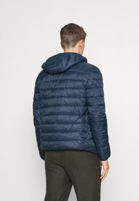 Doudoune bleu marine avec capuche, présentant des sections matelassées et une texture lisse et brillante. Détails de couture visibles sur les manches.