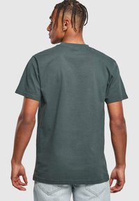 Mørkegrøn bomulds t-shirt med korte ærmer og rund hals, vist bagfra, som viser en glat tekstur og et enkelt design.