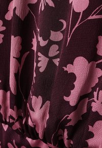 Gros plan sur un tissu texturé avec un motif floral violet foncé et rose et un détail froncé.