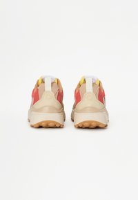 Sneakers with a beige upper, red and yellow accents, textured suede panels, and a rugged gum sole, featuring a pull tab at the heel.