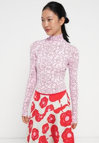 Vaalea pitkähihaine paita, jossa on kukkakuosi, korkea kaulus ja slim fit -malli. Yhdistetty valkoiseen hameeseen, jossa on suuria punaisia kukkia.