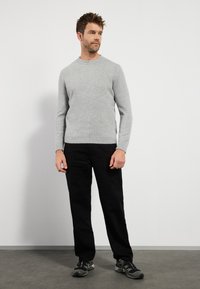 Light gray wool sweater with a round neckline, long sleeves, and ribbed cuffs, paired with black pants and dark athletic shoes.