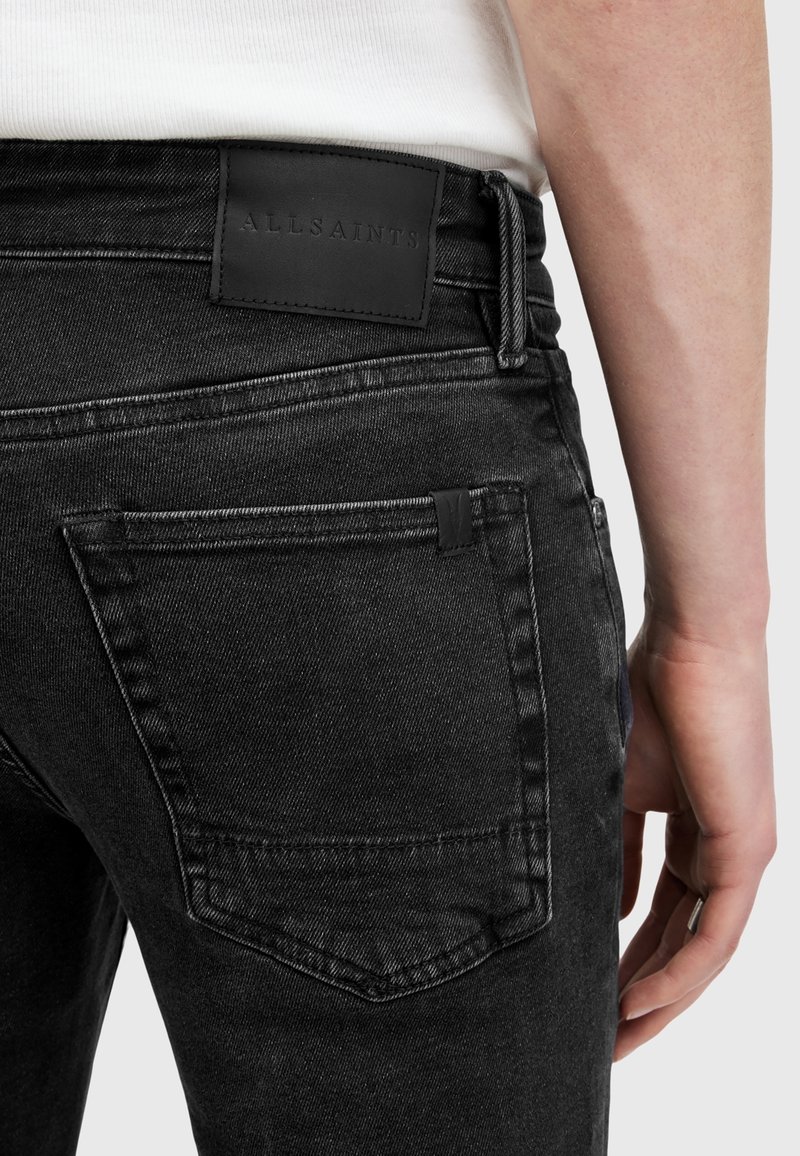 Černé džíny z denimu s texturovaným povrchem, se černou koženou nášivkou na pasu a dvěma zadními kapsami se švy.