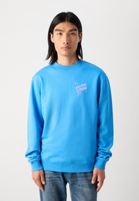 Blauwe crewneck sweatshirt gemaakt van katoen, met een klein roze logo op de borst, lange mouwen en een geribbelde halslijn en manchetten.