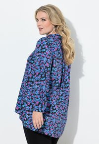 Blus med blå och lila blommönster, lång ärm, hög halsringning och lös passform, med en subtil drapering och mjuk textur.