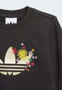 Juodas džemperis su apvalia iškirpte, puoštas ryškiomis rožinės, geltonos ir žalios spalvų siuvinėtomis gėlėmis aplink auksinį logotipą.