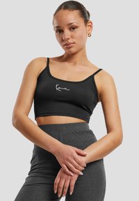 Black cropped tank top in stretchy fabric with thin straps and white logo detail on the front, paired with ribbed charcoal gray high-waisted pants.