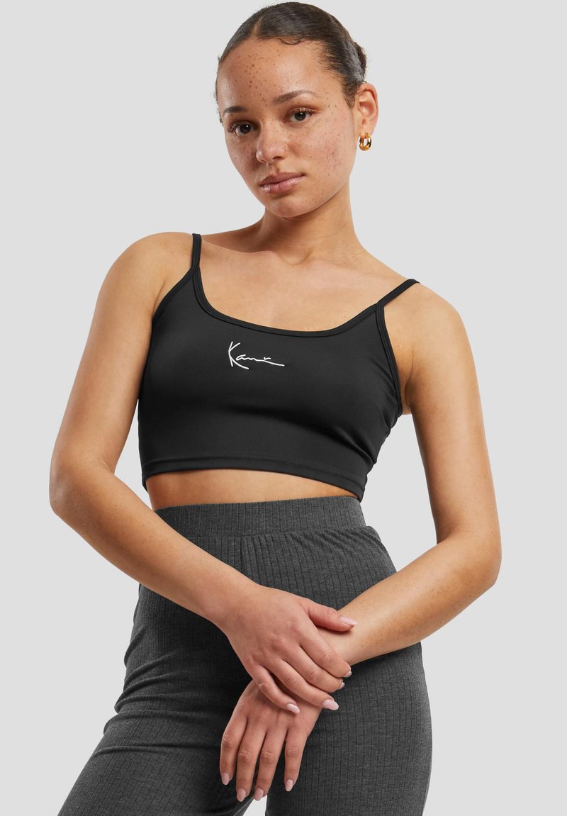 Black cropped tank top in stretchy fabric with thin straps and white logo detail on the front, paired with ribbed charcoal gray high-waisted pants.