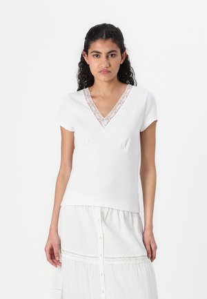 Hvit kortermet topp med V-hals, med blondekant og overlappende design. Myk tekstur, figursydd fasong og minimalistisk stil.