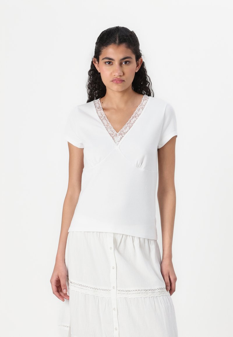 White short-sleeve top with a V-neckline, featuring a lace trim and an overlapping design. Soft texture, fitted shape, and minimalistic style.