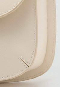 Primo piano dell'angolo di una borsa in pelle color crema con cuciture visibili e texture liscia.